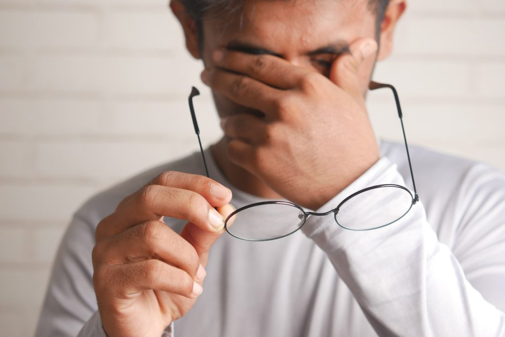 Man removing his glasses and covering his eyes as if they were itchy or he was crying.