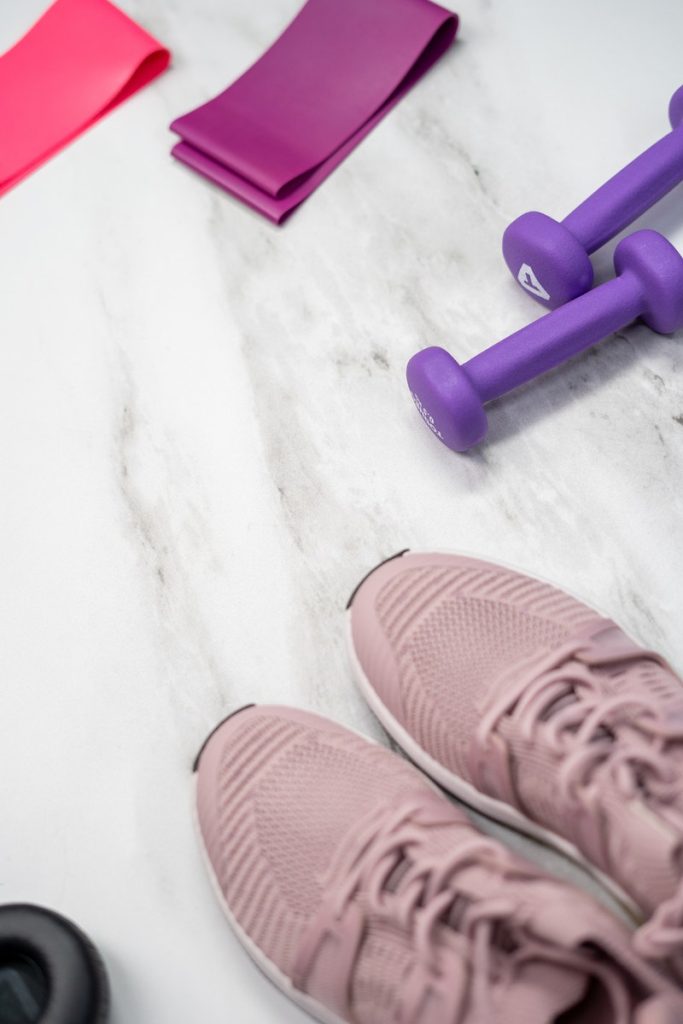Gym equipment and pink sneakers on white background