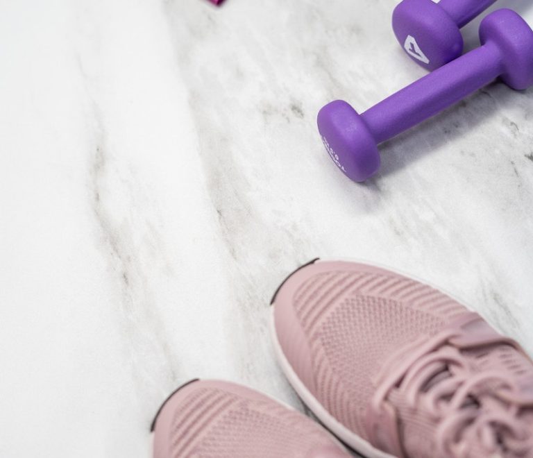 Gym equipment and pink sneakers on white background