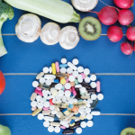 Assorted fruits, vegetables, and a pile of vitamins on a blue wooden table, representing healthy diet choices